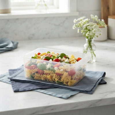 A clear airtight food storage container filled with pasta on a white marble countertop with slate blue linens and flowers.